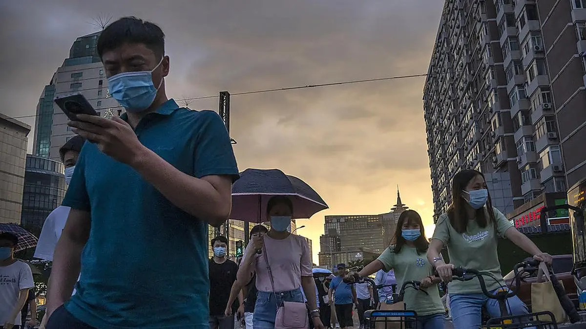 A man uses his smartphone as he walks across an intersection during the evening rush hour in Beijing, Thursday, Aug. 26, 2021. Chinese regulators will exercise greater control over the algorithms used by Chinese technology firms to personalize and recommend content, in the latest move in a regulation spree across the internet sector. The planned regulations could affect companies like ByteDance and Alibaba, which use algorithms to offer personalized services to users. (AP Photo/Mark Schiefelbein)
