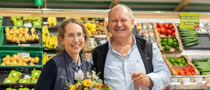 Zwei Menschen stehen in einem Lebensmittelgeschäft und lächeln in die Kamera 