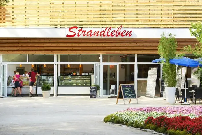 Café Restaurant Strandleben:
Von Anfang an bei der Pink Lake dabei ist Günther Wienerroither vom Café und Restaurant Strandleben direkt neben dem Pörtschacher Strandbad. Während der Festivalwoche wird das Lokal passend dekoriert, zudem ist das Strandleben heuer Gastgeber von zwei Veranstaltungen: einer Drag-Show und der Gayme Night. „Wir machen das von Anfang an und sind sehr gut damit gefahren“, sagt Wienerroither. Auch tagsüber ist sein Team eingebunden und betreut die Festivalgäste auf der Blumeninsel, wo sich der offizielle Treffpunkt befindet. Für den Gastronomen ist die LGBTQIA+-Community längst zu einem wichtigen Publikum geworden. „Die Gäste bringen auch Geld in die Region“, betont Wienerroither. Entscheidend sei für ihn aber, dass sich die Besucherinnen und Besucher willkommen fühlen – nicht nur während Pink Lake.
