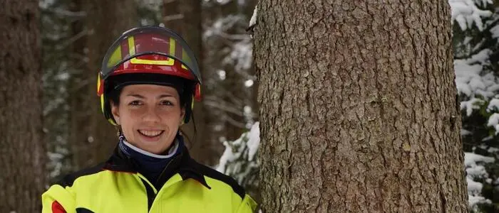 Man sieht eine Frau in Schutzkleidung mit Motorsäge neben einem Baum