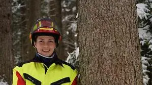 Man sieht eine Frau in Schutzkleidung mit Motorsäge neben einem Baum