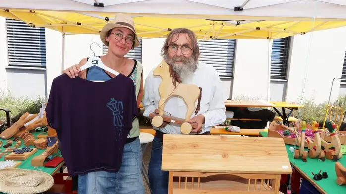 Marie Lenoble steht mit einem bedruckten T-Shirt in der Hand neben ihrem mittlerweile verstorbenen Vater Jean-Luc. Er hält ein Holzschaukelpferd in der Hand, das er selbst angefertigt hat.