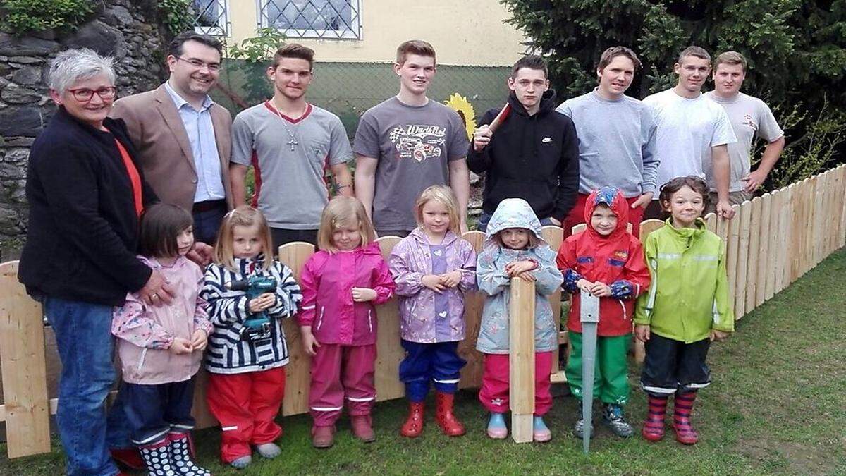 Die Kinder freuen sich gemeinsam mit Obmann Roland Mathiesl und der stv. Leiterin Gabi Loipold über den neuen Zaun von der FBS Zimmerei.