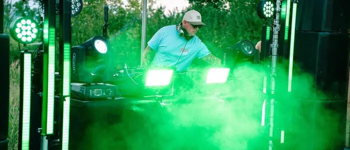 Ein DJ steht an einem Mischpult und ist von grünem Rauch umgeben