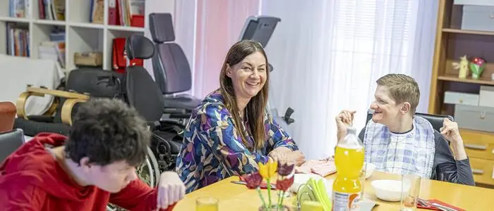 Drei Personen sitzen an einem gedeckten Tisch und essen gemeinsam