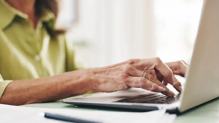 Die Hände einer älteren Frau tippen auf der Tastatur eines Laptops