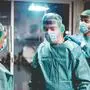 Doctors and nurse preparing to work in hospital for surgical operation during coronavirus pandemic outbreak - Medical workers getting dressed inside clinic - Focus on right man face