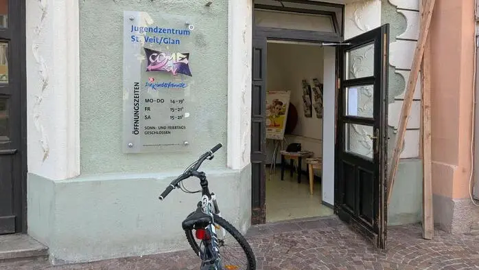 Außenansicht eines grünen Gebäudes, davor steht ein Fahrrad. Die Eingangstür ist offen.
