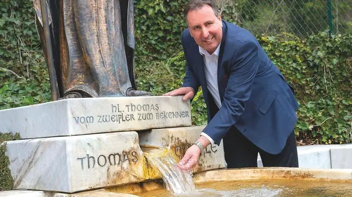 Ein Mann steht an einem Brunnen und hält seine Hand in den Wasserstrahl