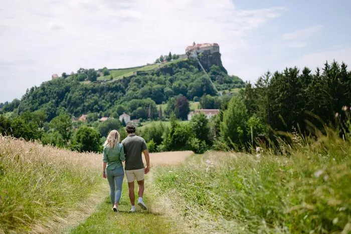 Ein paar geht auf einem Feldweg spazieren. Im Hintergrund ist die Riegersburg zu sehen.