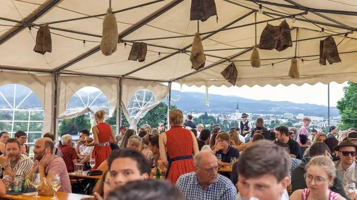 Blick in ein Kirchtagszelt, das gut gefüllt ist, im Hintergrund sieht man die Villacher Innenstadt