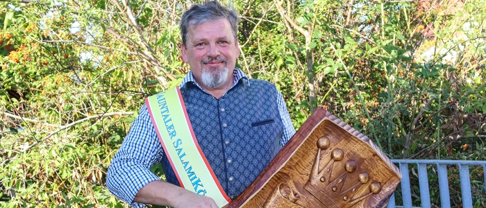 Ein Mann mit grauen Haaren und Bart hält eine Auszeichnung in der Hand