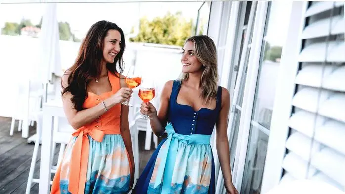 Zwei Frauen in moderner Tracht stoßen mit Gläsern an