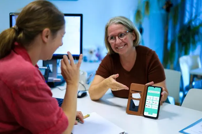 Zwei Frauen sitzen an einem Tisch, eine zeigt auf ihrem Handybildschirm die Notfall-App für Gehörlose.