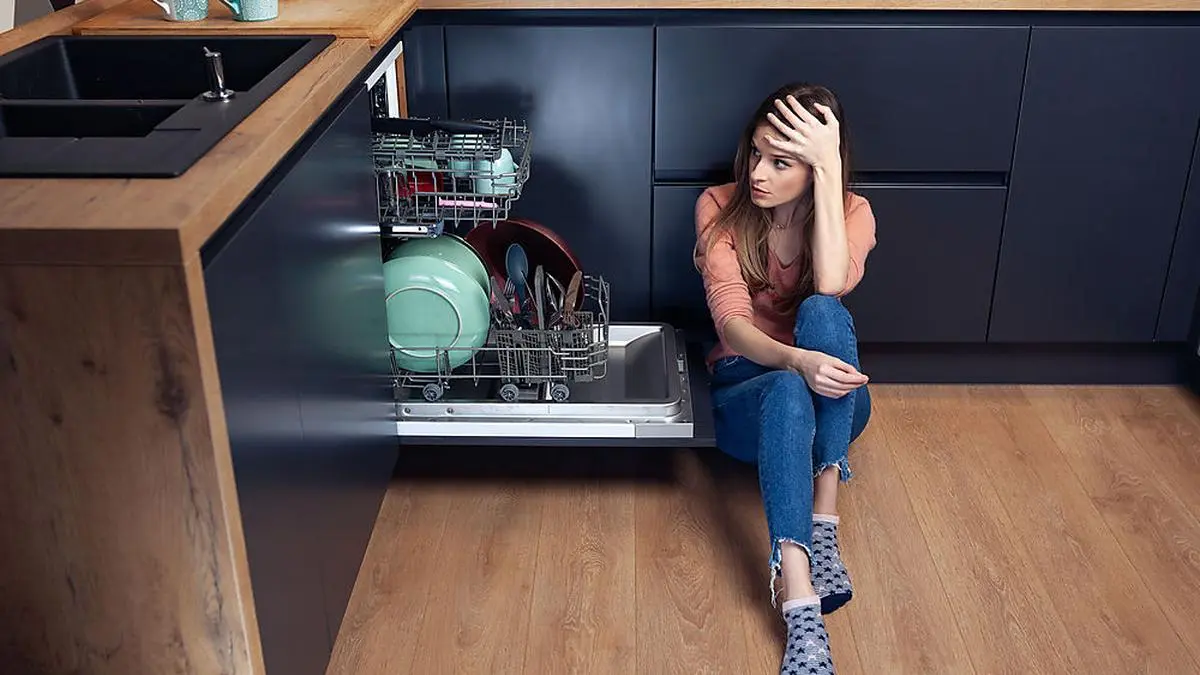 Beautiful young woman frustrated with dishes in a modern kitchen with dishwasher