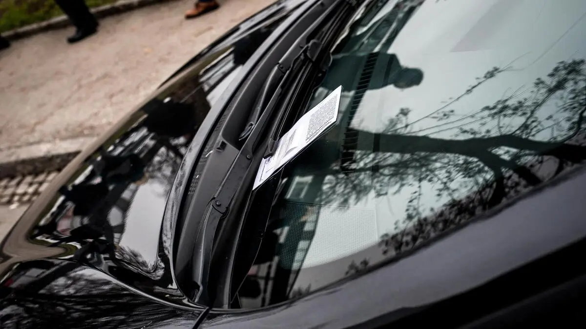 Ein Strafzettel liegt auf einer Windschutzscheibe eines schwarzen Autos | Parksünder können in Klagenfurt mehrmals täglich mit Strafzetteln bedacht werden