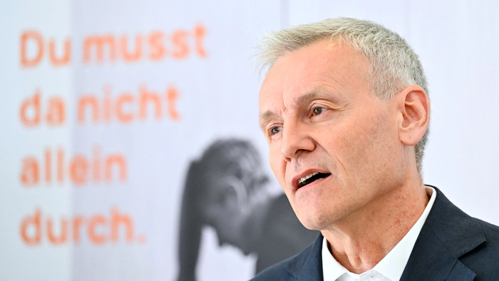 Ein Mann im dunklen Anzug und mit weißem Hemd, hinter ihm der Schriftzug „Du musst da nicht alleine durch“