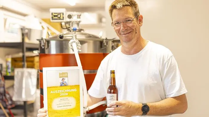 Gunther Kühnelt hält eine Urkunde und eine Bierflasche in der Hand und steht vor einem Braukessel