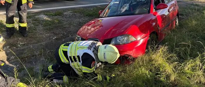 Ein roter Pkw im tiefen Straßengraben, davor gebückt arbeitend ein Kamerad der Feuerwehr Grafendorf