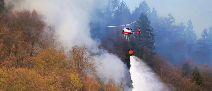 Ein Löschhubschrauber über einem rauchenden Wald