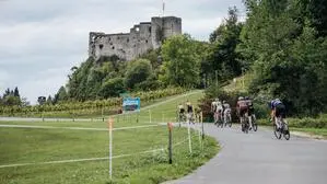 Mehrere Rennradfahrer fahren auf einer Straße, im Hintergrund erhebt sich eine Burg