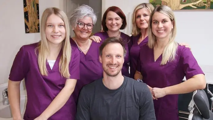 Ein Mann sitzt, hinter ihm stehen 5 Frauen