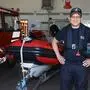 Ein Mann posiert in Feuerwehreinsatzuniform vor einem Einsatzboot für ein Foto.