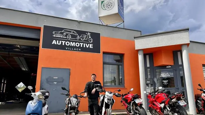 Ein junger Mann in schwarz gekleidet steht vor einer Autowerkstatt
