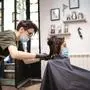 Hairdresser and girl child customer in a salon with medical masks during virus pandemic. Working with safety mask.