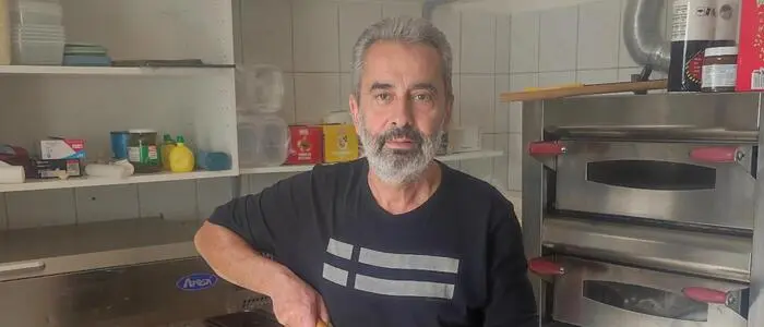 Ein Mann mit grauen Haaren und Bart hält eine Pizza auf einer Pizzaschaufel