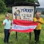 Die Einwohner der Türkei, Arno Felderer und Karl Binder stehen hinter Österreich und vor der Ortstafel „Türkei“