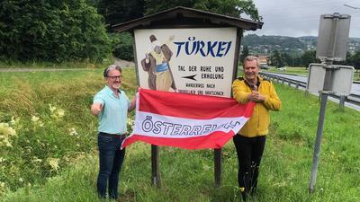 Die Einwohner der Türkei, Arno Felderer und Karl Binder stehen hinter Österreich und vor der Ortstafel „Türkei“
