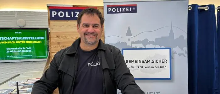 Ein Mann lacht in die Kamera. Hinter ihm sind mehrere Polizeibanner.