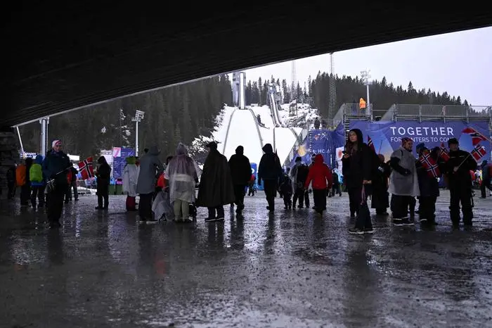 Visitors take shelter from the rain under a bridge as the ski jumping slopes are seen in the background, during the FIS Nordic World Ski Championships in Trondheim, Norway on March 2, 2025.  (Photo by Jonathan NACKSTRAND / AFP)