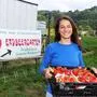 Eine Frau mit einer Kiste voller Erdbeeren lächelt in die Kamera
