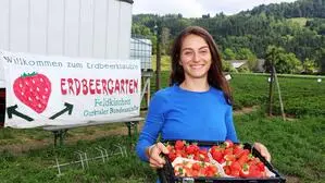 Eine Frau mit einer Kiste voller Erdbeeren lächelt in die Kamera