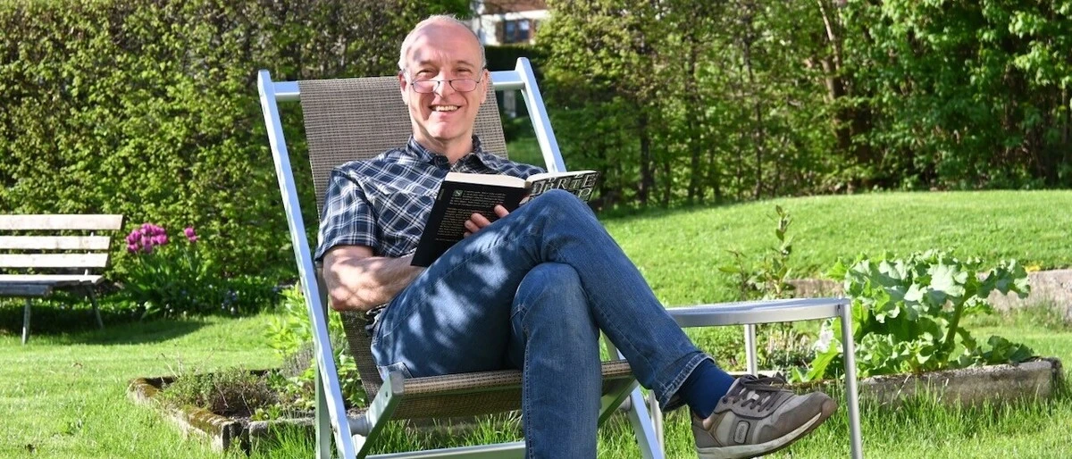 Dieter Mayr-Hassler sitzt in einem Stuhl vor seinem Hotel und liest ein Buch