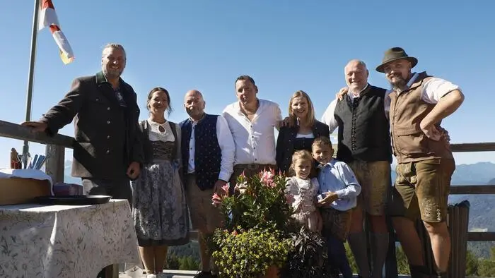 Eine Gruppe von Männern und Frauen in Tracht steht auf der Terrasse einer Almhütte