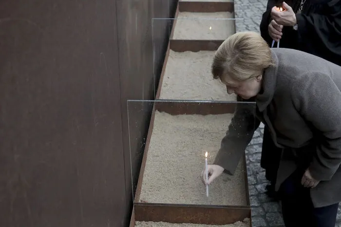 Bundeskanzlerin stellt eine Kerze am Mauer-Denkmal auf.
