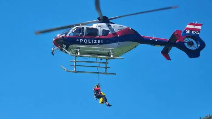 Eine Person hängt an einem Tau, das von einem Polizeihubschrauber herabhängt.