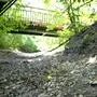 Ausgetrocknetes Flussbett in einem Waldstück, über das eine Brücke führt.