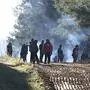 Belarusian soldiers, left, stand guard as migrants from the Middle East and elsewhere gather at the Belarus-Poland border near Grodno, Belarus, Tuesday, Nov. 9, 2021. Polish riot police and coils of razor wire faced off Tuesday against migrants, including families with young children, who were camped just across the border in Belarus, amid a tense standoff on the European Union's eastern border. (Leonid Shcheglov/BelTA via AP)