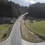 Drohnenaufnahme einer Straße die in einem Wald mündet. Links und rechts sieht man Wiese