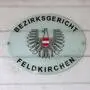 Ein Schild hängt an einer Wand. Darauf steht: „Bezirksgericht Feldkirchen“.
