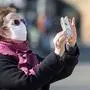 A woman wearing a protective mask takes pictures with her smartphone on an empty Alexanderplatz in Berlin on March 31, 2020 as the people in the German capital continue to observe a partial lock down to fight the Covid-19 corona virus pandemic. (Photo by Odd ANDERSEN / AFP)