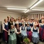 Zahlreiche Damen und Herren sitzen in Tracht nebeneinander 
