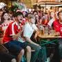Public Viewing beleben die Grazer Gastronomie: Foto zeigt Fußballfans auf Bierbänken, teils in Österreich-Trikots und Schals; ein Fan ballt die Faust und schreit, als würde er gerade zum Torjubel ansetzen