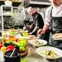 Professional chef cooking in the kitchen restaurant at the hotel, preparing dinner. A cook in an apron makes a salad of vegetables and pizza