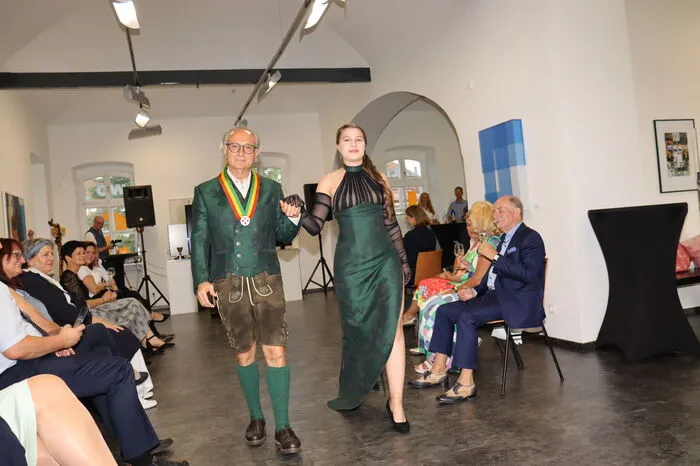 Um den Bogen, von der Bearbeitung von Boden und der Erzeugung von Bio-Wein zur Kleidung zu schaffen, benötigt es den passenden Stoff. Dieser Stoff, designed durch Josef Gerhard Pfleger in der Steiermark und gewebt in Vorarlberg, bringt ebenfalls die biologische Eigenschaft mit. Das GOTS-Zertifikat für giftfrei hergestellten Stoff stellt die erste Anbindung zum biologisch erzeugten Wein dar. Ein weiterer Anknüpfungspunkt ist das Motiv der gezeigten Stoffe, das sowohl typisch steirische und regionale Weststeirische Muster aufweist. Der steirische Panther, das Weinlaub und die edlen Pferde wurden ausgesucht, um der Sinn-phonie, in den zum Wein passenden Farben, die Basis zu geben.