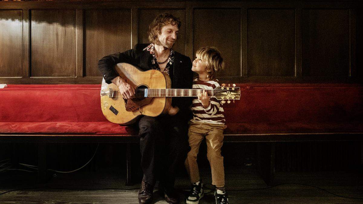 Voodoo Jürgens und Ben Winkler als Vater und Sohn in „Rickerl“ | Voodoo Jürgens und Ben Winkler sitzen auf einem roten Sofa - mit Gitarre